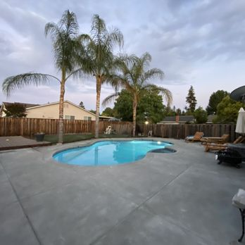 A serene backyard pool surrounded by palm trees and a wooden fence, showcasing the quality of Olivera Pool Services in San Jose.